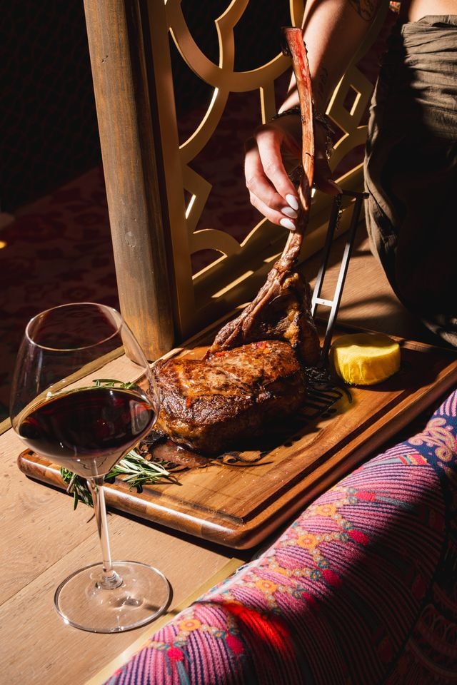 Grilled tomahawk steak carved tableside with red wine at Habibi Miami