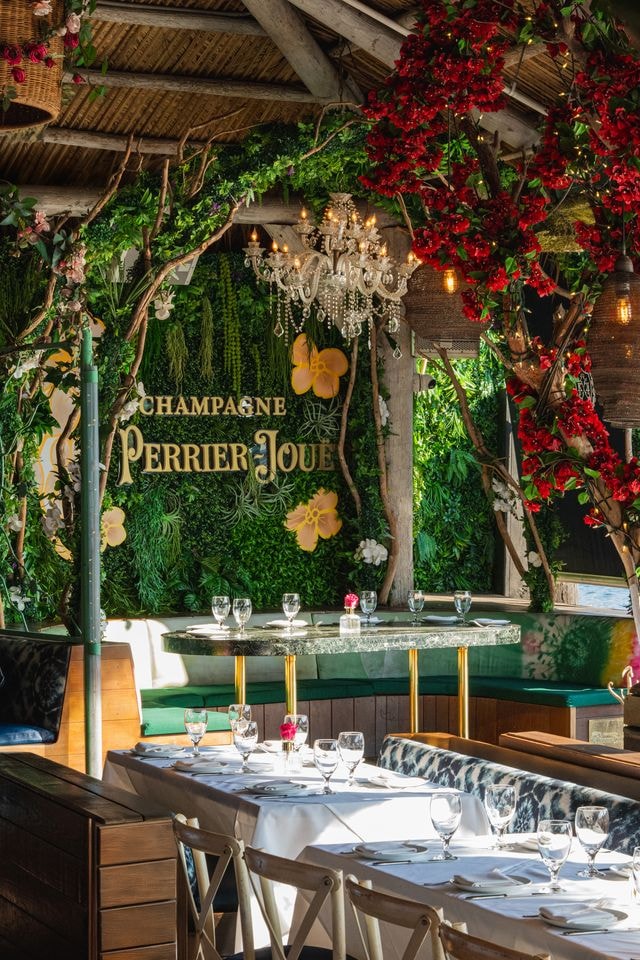 Kiki on the River interior with Perrier-Jouet champagne wall, crystal chandelier, and red flowers