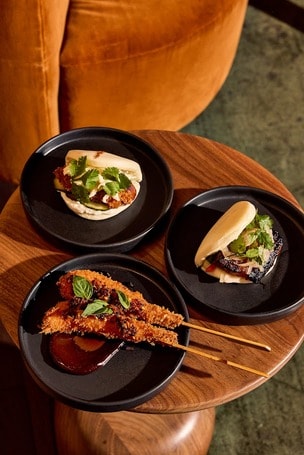 Uchibā small plates including bao and skewers on black plates