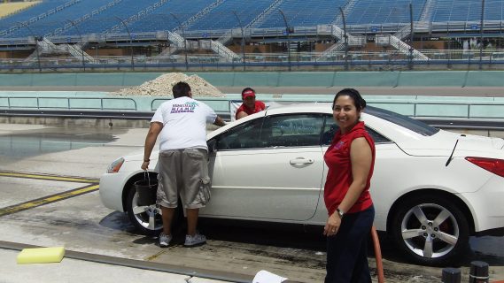 Homestead-Miami Speedway Accounts Payable and Accounts Receivable Clerk Sandy Arroyave waits to rinse off a car at the beginning of the event held on Coca-Cola Pit Road (also pictured Homestead-Miami Speedway Promotions Manager Randall Hoppe and Juanita Lopez Homestead-Miami Speedway Assistant to the Track President)