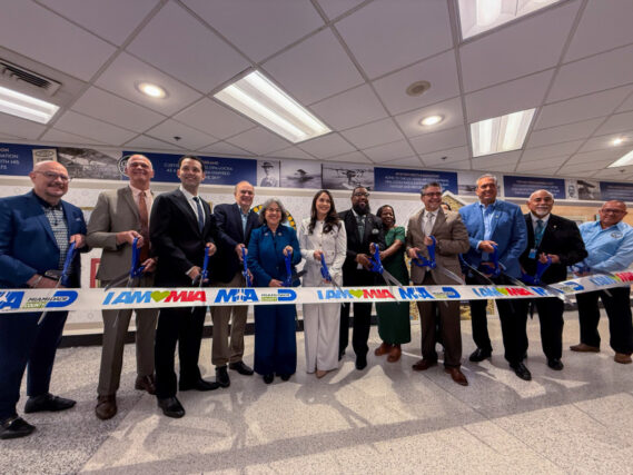 Miami-Dade County Mayor Daniella Levine Cava (left of center), County Commissioner Natalie Milian-Orbis (center), County Commissioner J.C. Bermudez (second left of center), MIA Director and CEO Ralph Cutié (second to left), and other officials from Miami-Dade County, the cities of Hialeah, Miami Springs, and Opa-locka, and the Greater Miami Convention and Visitors Bureau cut the ribbon at the new mural, From Wings to Cities: The Vision of Glenn Curtiss.